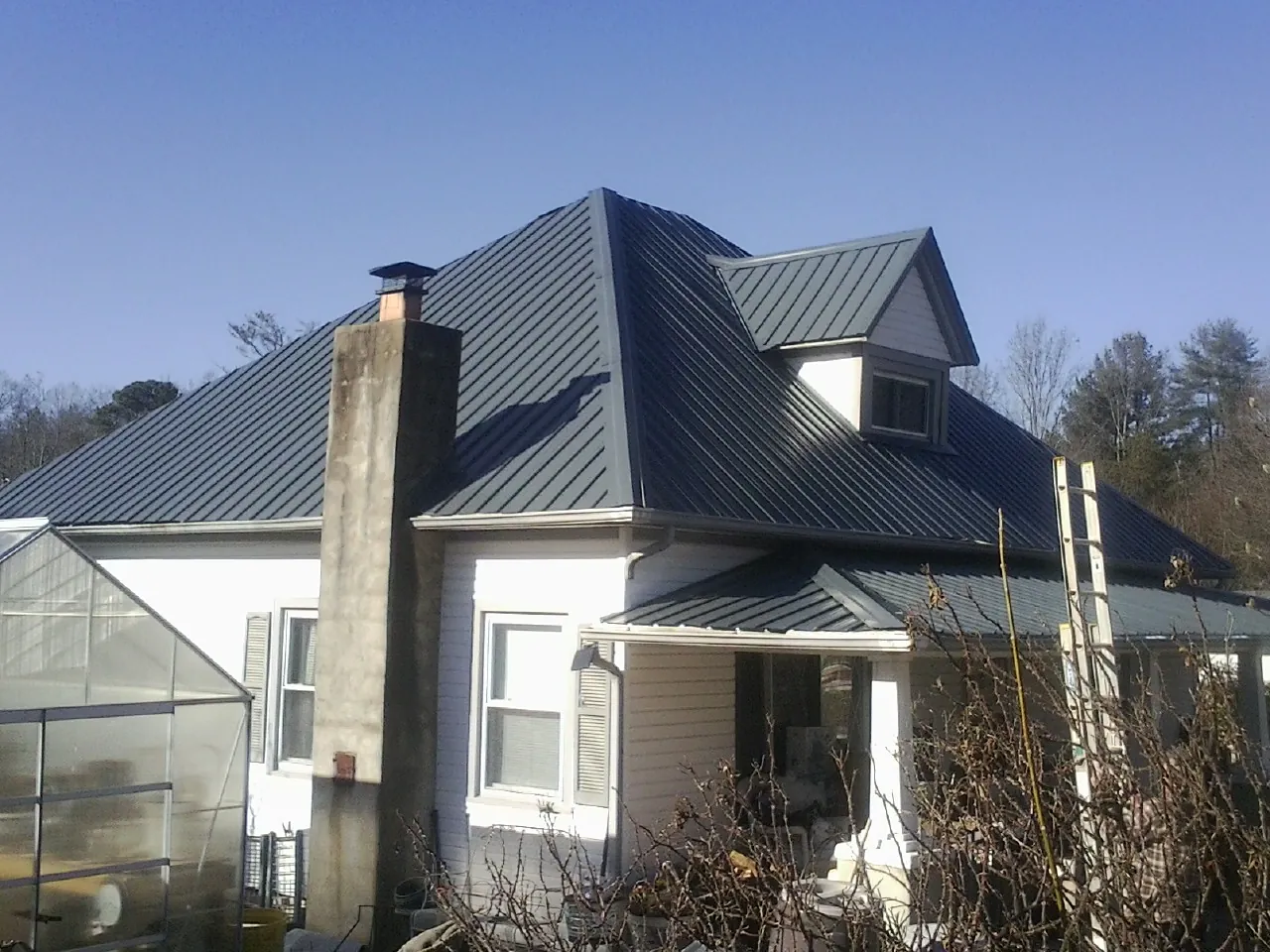 Dark blue standing seam metal roof on a white farmhouse with dormer — Slate & Tile Roof Repair by Roofing Brothers in Riverton