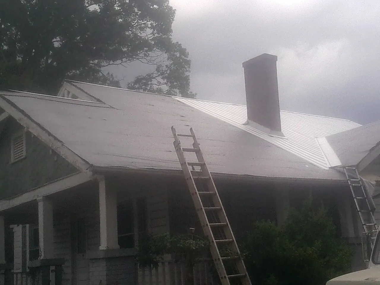 Ladders against a metal roof on an older home with a brick chimney in Riverton