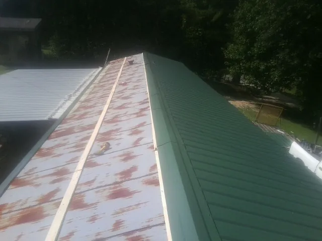 Old rusted panels beside newly installed green metal roofing — Wind Damage Roof Repair by Roofing Brothers in Riverton